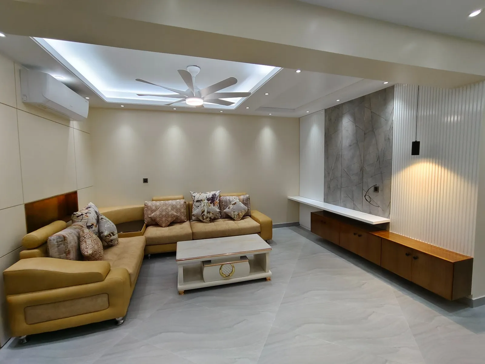 Living room with beige corner sofa, decorative cushions, white coffee table, and modern wall design
